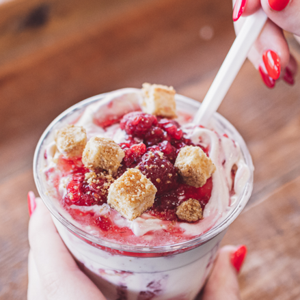 Hand holding a dessert cup with Raspberry and cheeecake on a wooden surface