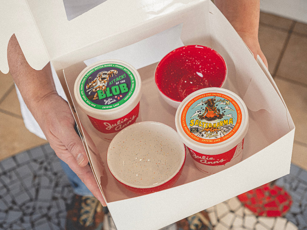 Four small containers with colorful labels in a white box, held by a person.