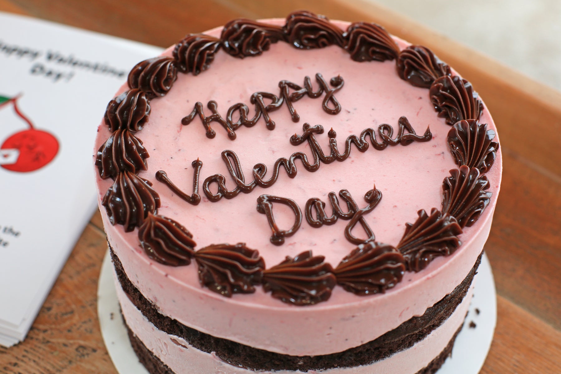 Pink cake with 'Happy Valentine's Day' text on a wooden surface