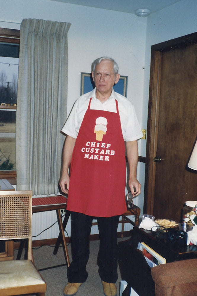 The late John Zielnicki wearing a red apron with 'Chief Custard Maker' in his living room.
